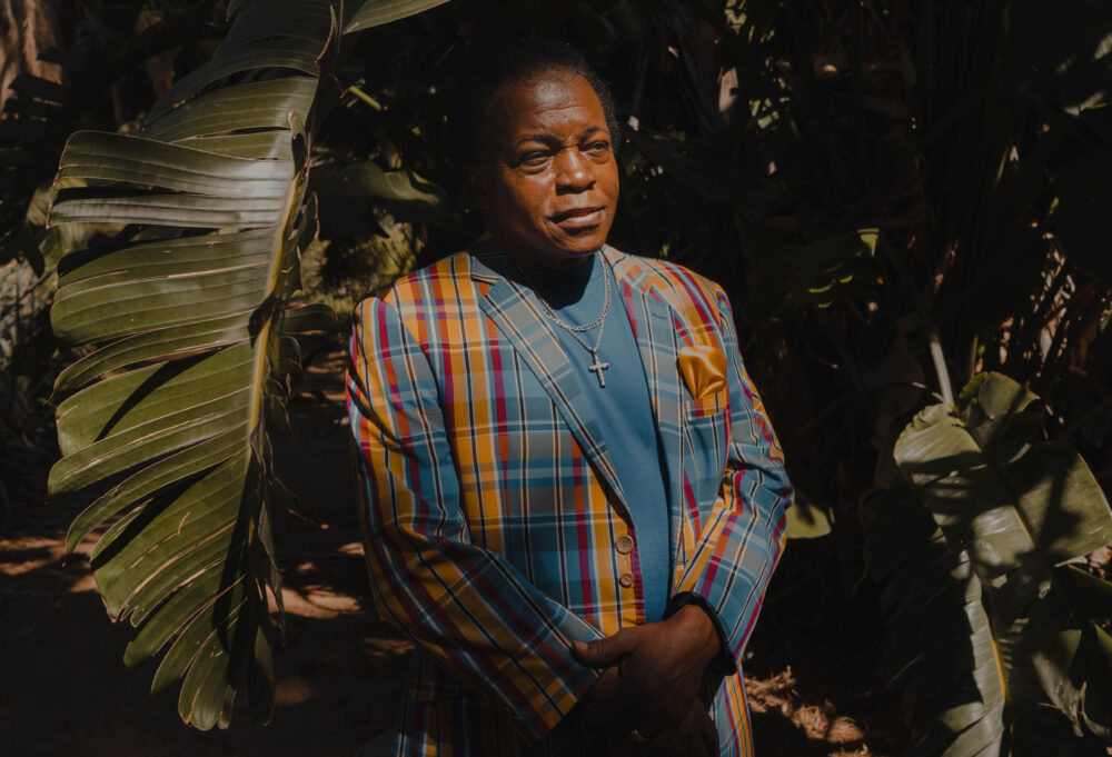 Portrait avec des plantes tropicales en arrière plan. Le sujet a un costume coloré.