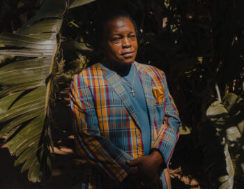 Portrait avec des plantes tropicales en arrière plan. Le sujet a un costume coloré.