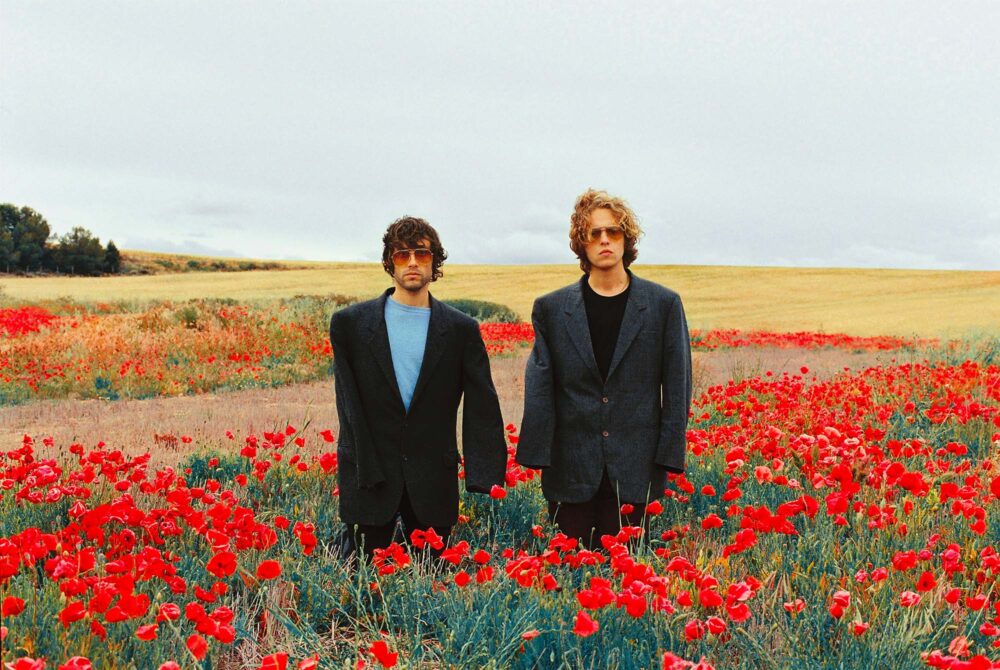 Portrait des deux artistes dans un champ de coquelicot. Ils ont des costumes trop grands, on ne voit pas leurs mains.