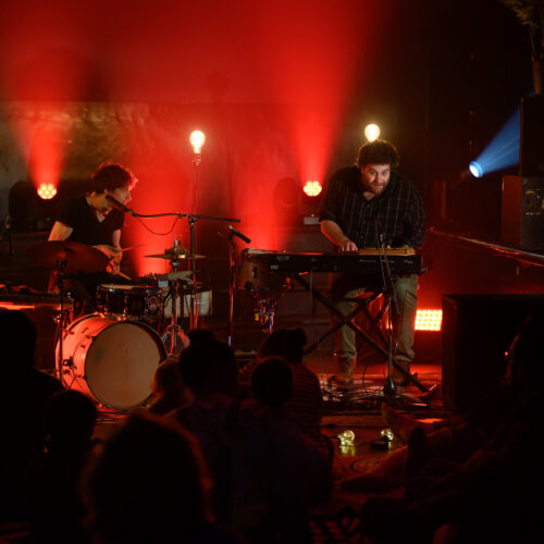 Les musiciens jouent de la batterie et du clavier sur scène dans une lumière rouge