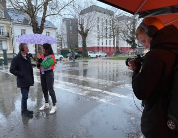 Deux jeunes interviewent une personne sous la pluie