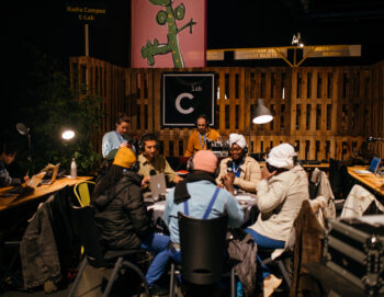 Photo de nuit en extérieur avec plusieurs personnes autours d'une table avec casques et micro. un homme est à une console son