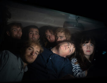 Plusieurs personnes posant entassées dans une voiture, on les voit à travers le pare-brise juste éclairées par le lumière de courtoisie