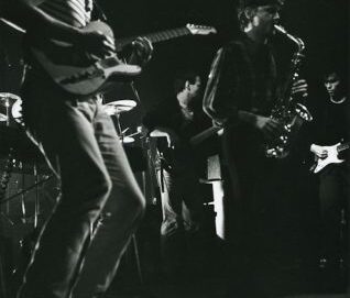Photo de concert en noir et blanc avec un saxophoniste et trois guitaristes