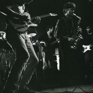Photo de concert en noir et blanc avec un saxophoniste et trois guitaristes