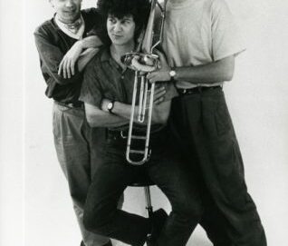 Portrait en noir et blanc d'un trio d'artiste dont l'un tient un trombone