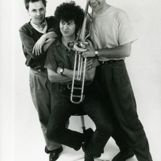 Portrait en noir et blanc d'un trio d'artiste dont l'un tient un trombone