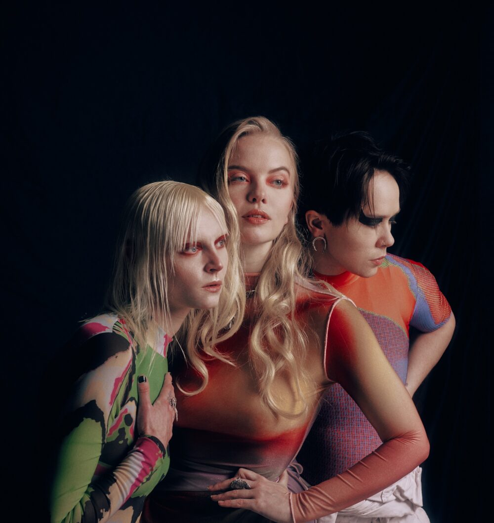 Portrait en clair obscur des trois artistes maquillés et habillés de manière très graphique et colorée