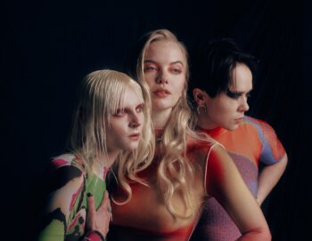 Portrait en clair obscur des trois artistes maquillés et habillés de manière très graphique et colorée