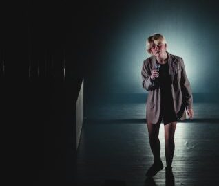 la chanteuse tient un micro, la pièce est noire, un projecteur n'éclaire que sa personne