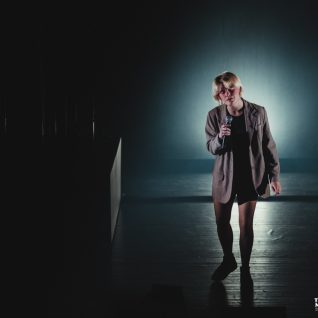 la chanteuse tient un micro, la pièce est noire, un projecteur n'éclaire que sa personne