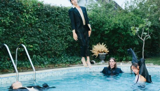 Photo assez floue de quatre hommes en costume dans une piscine dont un en plein saut