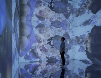 un homme observe le mur d'une salle dans laquelle une image est projetée sur toutes ses surfaces
