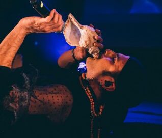 une personne allongée souffle dans un coquillage et tient un micro devant lui