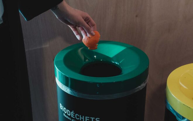gros plan d'une main qui jette une pelure de mandarine dans une poubelle de biodéchets