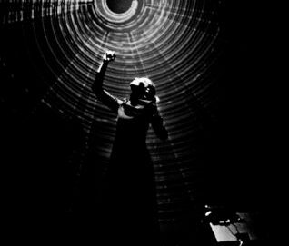 Photo noir et blanc de style clair obscur montrant une femme qui tend la main vers une lumière tournante