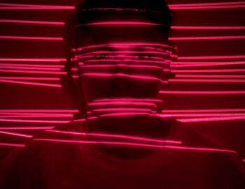 Portrait d'un personne dans le noir éclairée par de fins traits de lumière fuchsia horizontaux