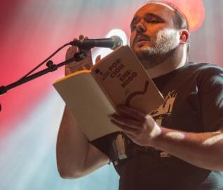 Un homme avec le visage devant un micro et tenant un livre dans sa main