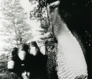 Un homme pose sous la patte d'une statue géante en forme de reptile