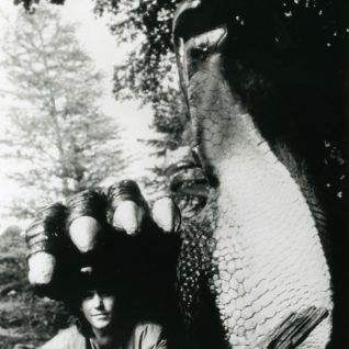 Un homme pose sous la patte d'une statue géante en forme de reptile