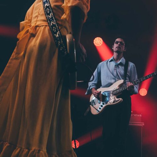 une guitariste femme en robe jaune de dos , face à un bassiste