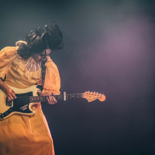 Une guitariste avec une robe longue jaune romantique et les cheveux en mouvement
