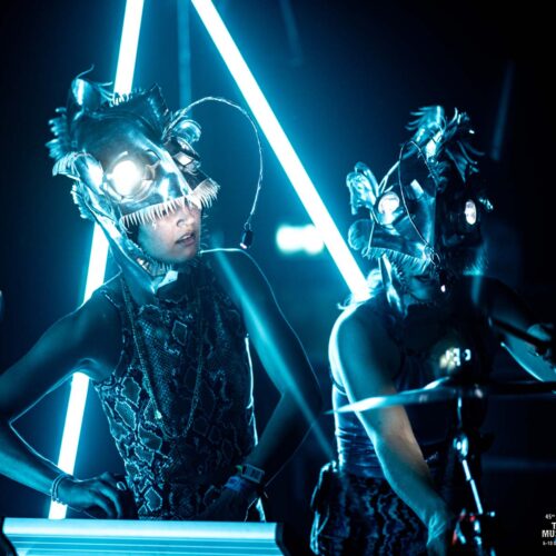 Deus artistes féminines performant avec des cagoules argentées en forme de tête de poissons à lumières