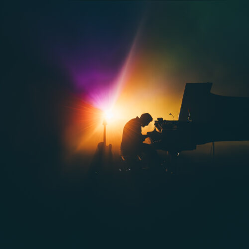 Un pianiste en contre jour avec une lumière vive et colorée derrière lui