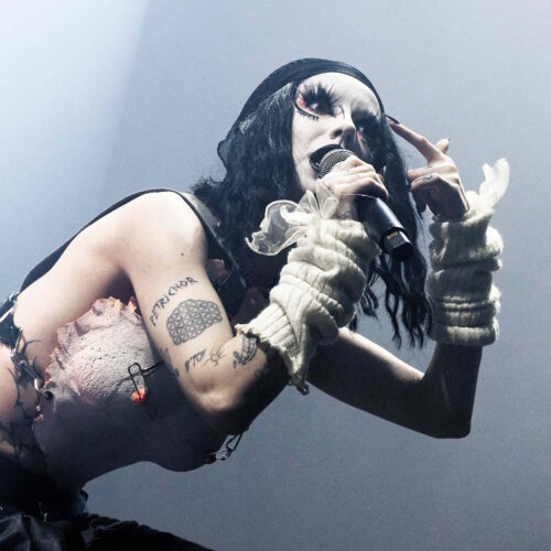Une artiste a la tenue dark chante en pointant son visage du doigt