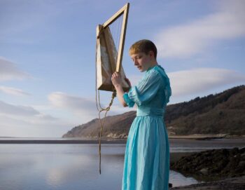 Une jeune femme tient une harpe, elle est sur la plage