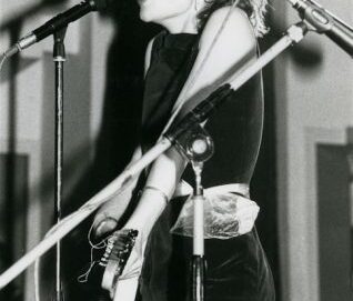 Photo en noir et blanc d'une chanteuse criant dans le micro, la photo est coupée au niveau de la bouche.