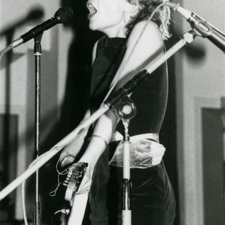 Photo en noir et blanc d'une chanteuse criant dans le micro, la photo est coupée au niveau de la bouche.