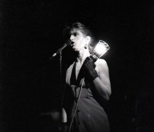 Photo en noir et blanc d'une chanteuse tenant une lampe baladeuse à côté du micro