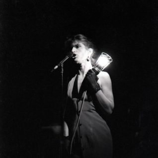 Photo en noir et blanc d'une chanteuse tenant une lampe baladeuse à côté du micro