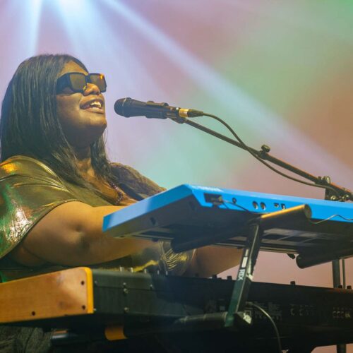 Une artiste chantant et jouant du clavier tête haute et lunettes de soleil