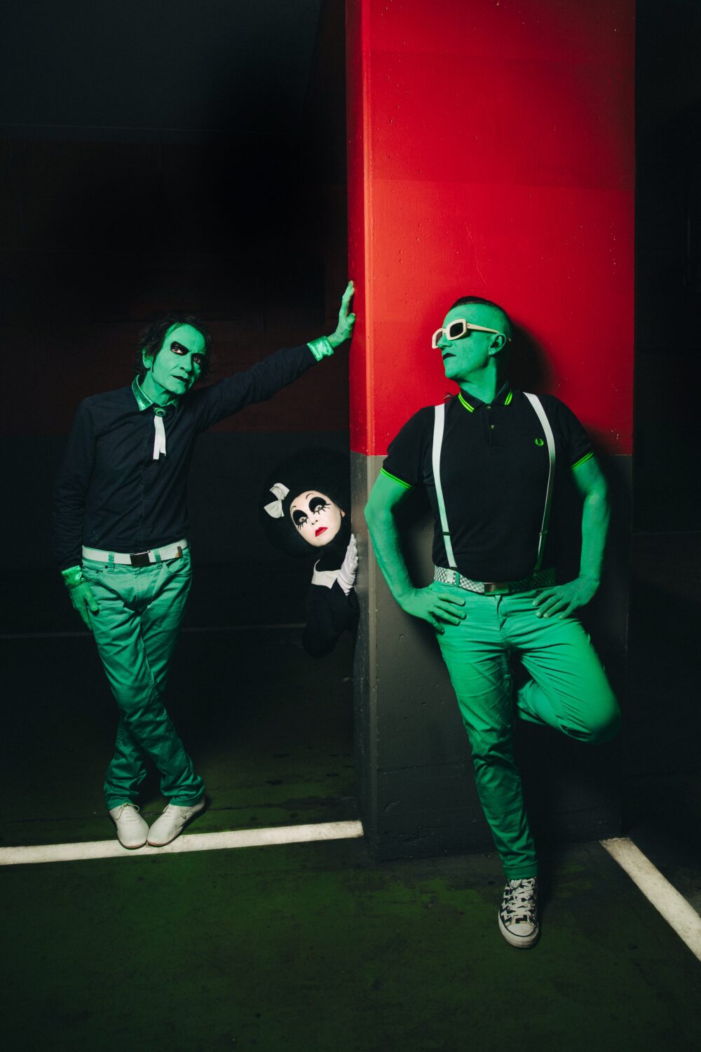 Trois artistes posant dans une lumière verte sur fond rouge et noir